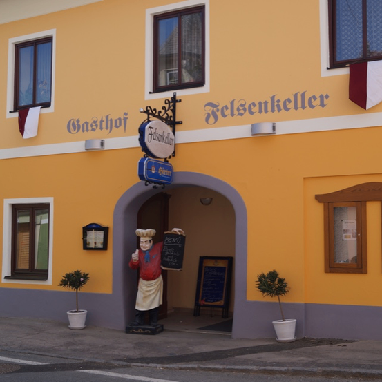 Ein gelbes Gebäude mit dem Namen Felsenkeller oben. Vor dem Eingang steht eine Statue eines Kochs. Auf beiden Seiten des Eingangs stehen zwei Topfpflanzen.