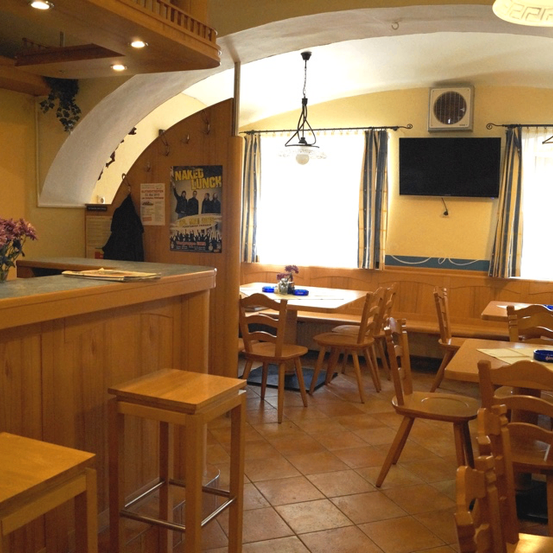 Das Innere eines gemütlichen Restaurants mit Holzmöbeln, einer Theke, einem montierten Fernseher und einem mit Blumen geschmückten Tisch.