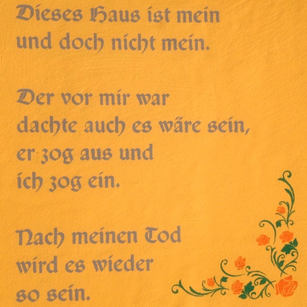 Ein gelber Hintergrund mit deutschem Text, der in einer kursiven Schrift geschrieben ist. Der Text lautet: Dieses Haus ist mein und doch nicht mein. Der vor mir war, dachte auch, es wäre sein, er zog aus und ich zog ein. Nach meinem Tod wird es wieder so sein.