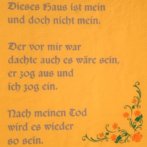Ein gelber Hintergrund mit deutschem Text, der in einer kursiven Schrift geschrieben ist. Der Text lautet: Dieses Haus ist mein und doch nicht mein. Der vor mir war, dachte auch, es wäre sein, er zog aus und ich zog ein. Nach meinem Tod wird es wieder so sein.