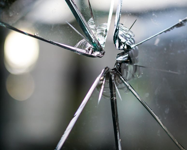 Nahaufnahme eines zerbrochenen Glasfensters mit scharfen, zerklüfteten Kanten und einem zentralen Aufprallpunkt.