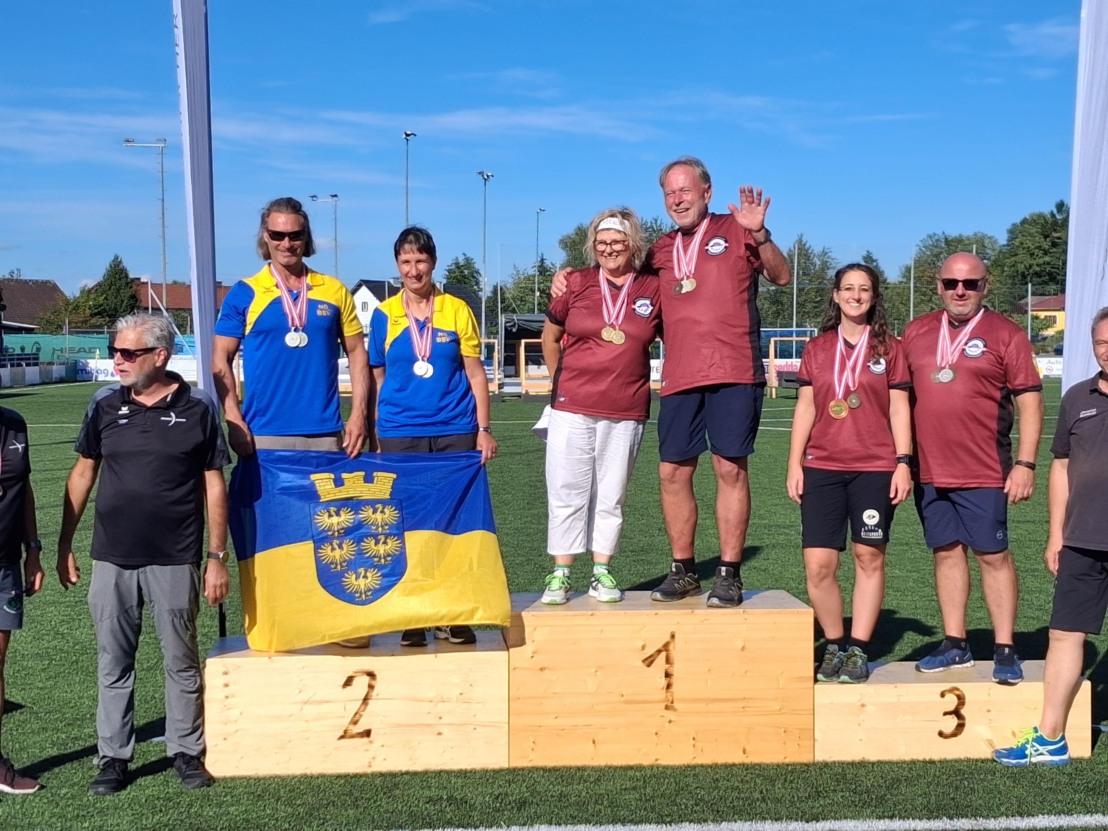 Siegerehrung mit Medaillen und Fahne auf Podest vor blauem Himmel