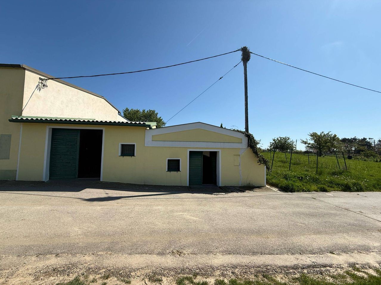 Ein gelbes Gebäude mit einem grünen Dach und grünen Türen, gelegen an einer Straße mit einem grasigen Feld im Hintergrund.