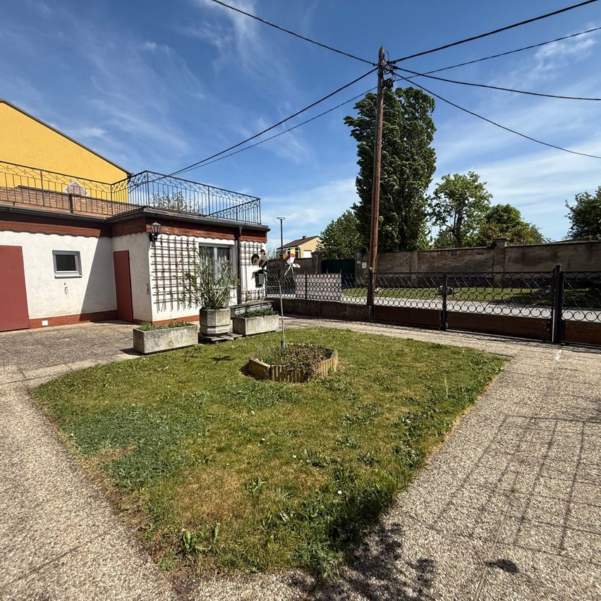 Ein Haus mit Balkon, kleinem Garten und Zaun. Das Haus hat rote und weiße Wände.