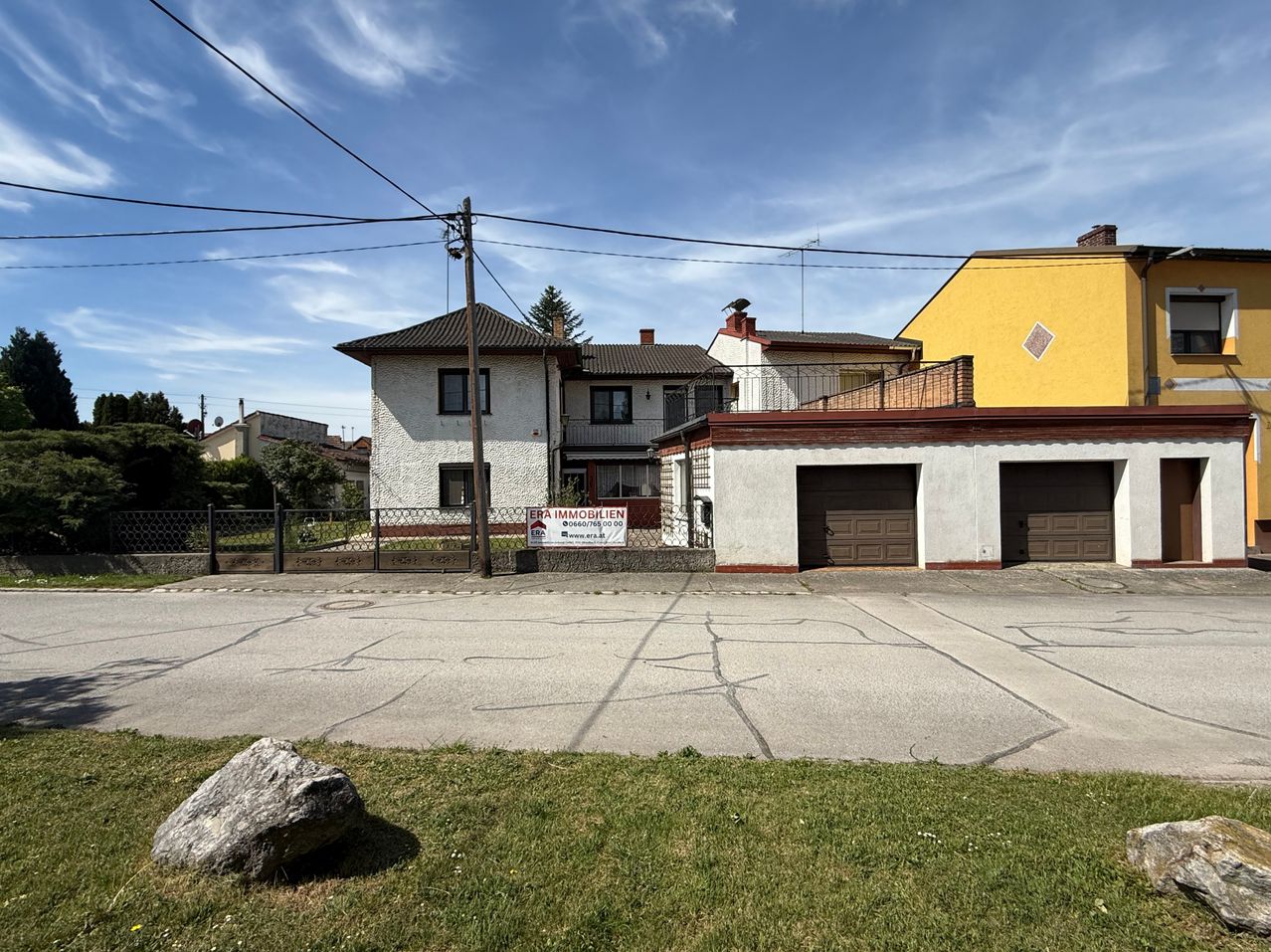 Ein Haus mit einer großen Garage davor, ein Schild davor und ein Rasenbereich mit einem Stein in der Nähe.