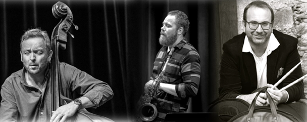 Drei Musiker in Schwarz-Weiß posieren für ein Foto. Der linke spielt Cello, der mittlere spielt Saxophon und der rechte hält Drumsticks.