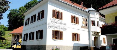 Ein weißes Gebäude mit braunen Fensterläden und einer Wandmalerei. Ein gelber Lieferwagen ist in der Nähe geparkt.