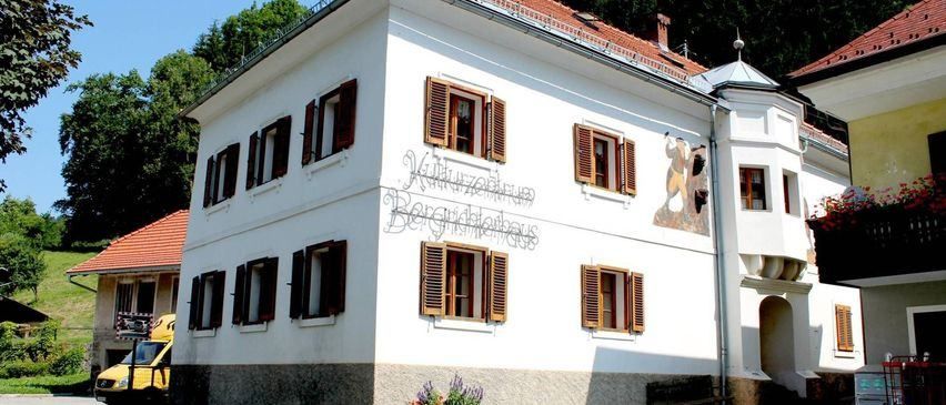 Ein großes weißes Gebäude mit braunen Fensterläden hat eine Wandmalerei eines Mannes und einer Frau an der Seite. Vor dem Gebäude ist ein gelber Lieferwagen geparkt.