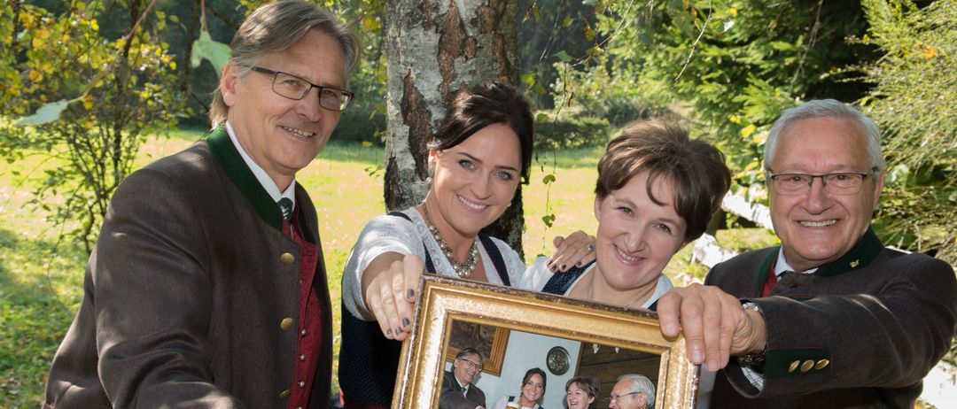 Vier Personen stehen draußen und halten einen Bilderrahmen mit einer Gruppe in einer Bar. Sie alle lächeln.