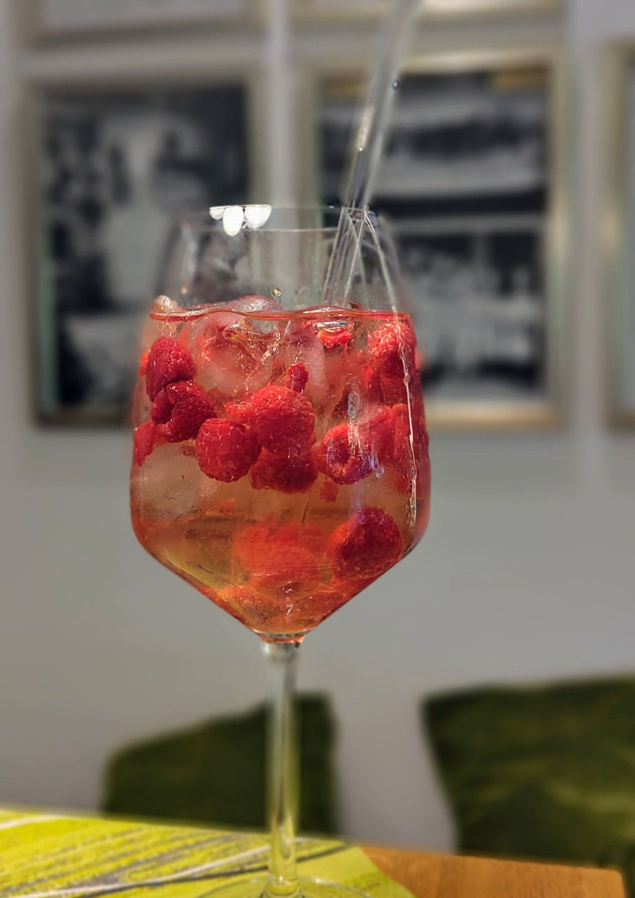 Ein Weinglas mit einem erfrischenden Getränk gefüllt, gekühlt mit Eis und dekoriert mit frischen Himbeeren, auf einem Tisch platziert.