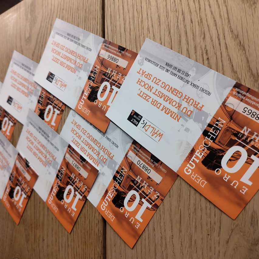 Ein Stapel orangefarbener und weißer Tickets mit dem Text 'Tickets für das Musical' und anderem Text auf einem Holztisch.