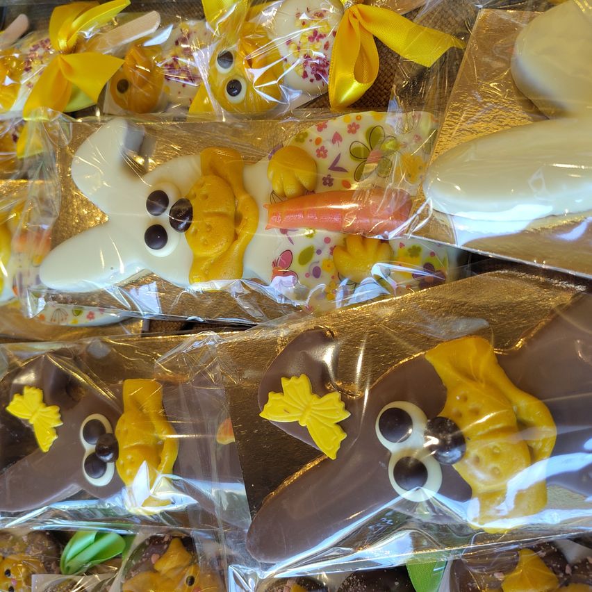 Eine Ausstellung von Schokoladen-Osterhasen, einzeln in Klarsichtfolie verpackt. Jeder Hase hat gelbe Schleifen und Ohren, einige halten eine Karotte. Die Schokolade ist eine Mischung aus weiß, gelb und braun.