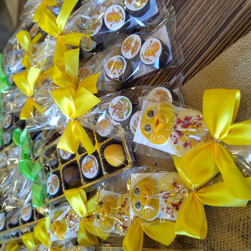 Mehrere Sets von Desserts, jedes in Plastik mit gelben Schleifen verpackt, sind auf einer Holzoberfläche angeordnet. Jedes Set enthält verschiedene Süßigkeiten und ein gelbes Ei. Einige Süßigkeiten haben Löwendesigns.