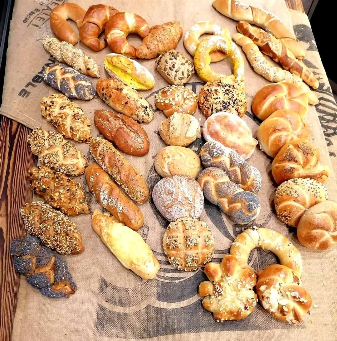 A variety of breads and rolls are arranged on a burlap cloth, including bagels, pretzels, and breadsticks.