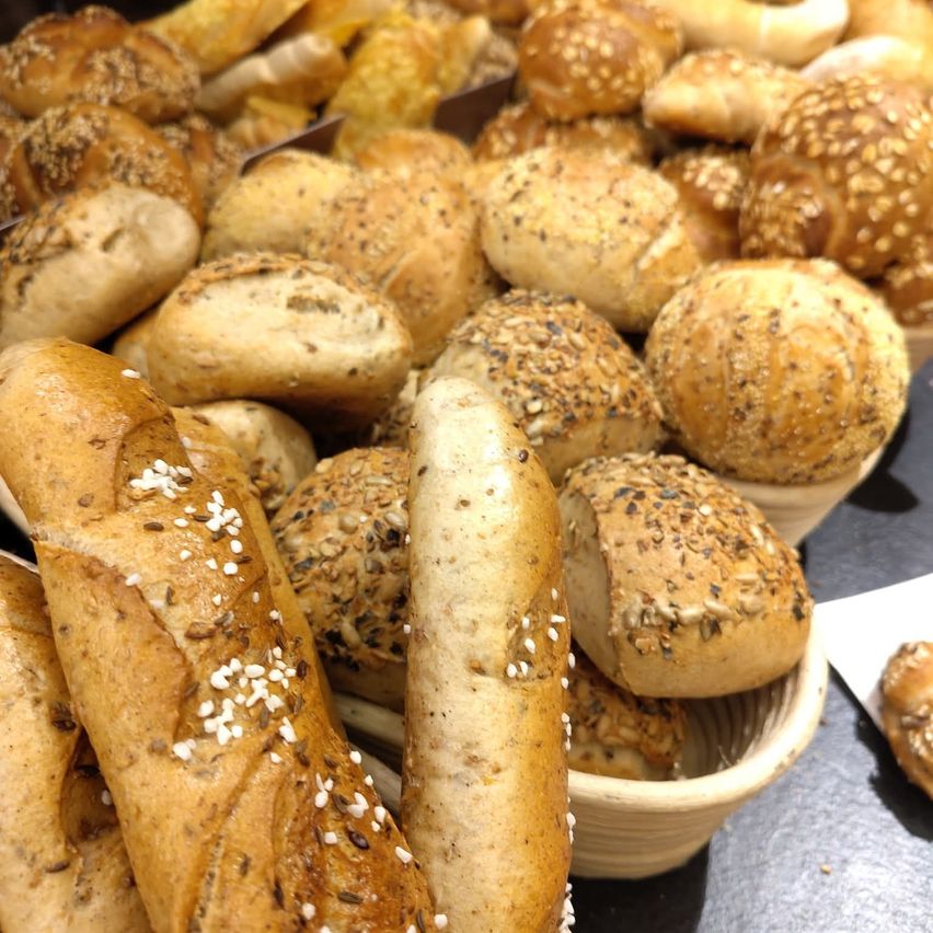 A close-up view of a variety of freshly baked bread rolls with sesame seeds and other toppings, arranged on a table.