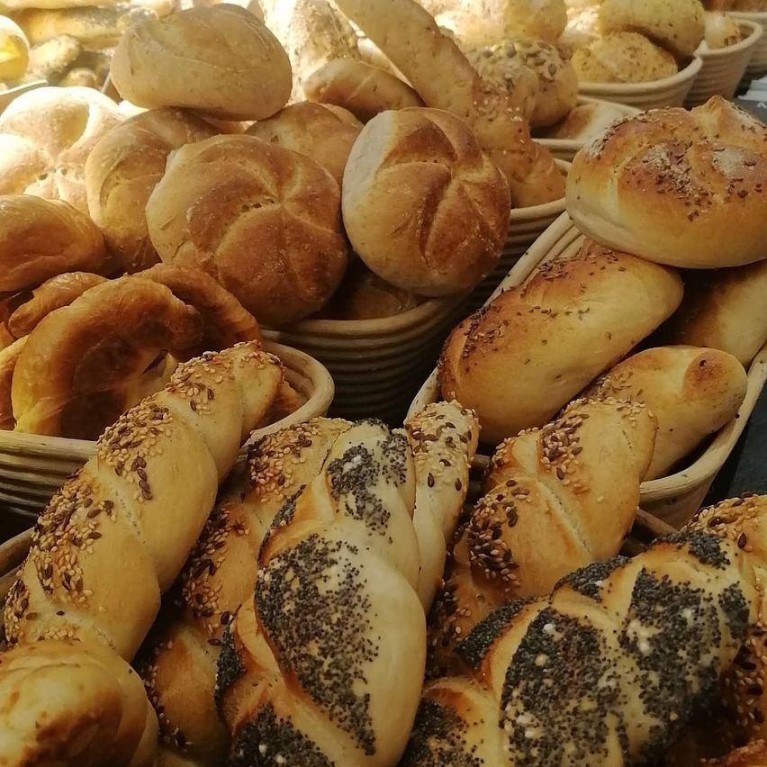 A variety of breads including round loaves, rolls, and long loaves with sesame and poppy seeds are displayed in baskets.