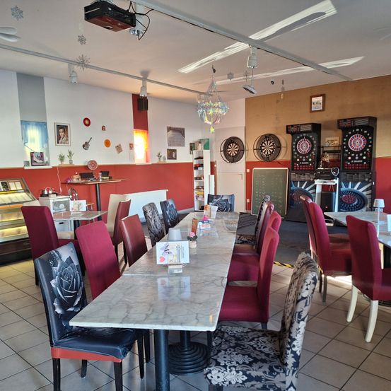 Ein Restaurant mit einem langen Marmortisch und roten Stühlen, mit Dart-Maschinen, einer Tafel und verschiedenen Dekorationen an den Wänden.
