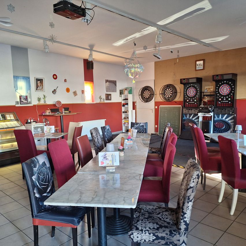 Ein Restaurant mit einem langen Marmortisch und roten Stühlen, mit Dart-Maschinen, einer Tafel und verschiedenen Dekorationen an den Wänden.