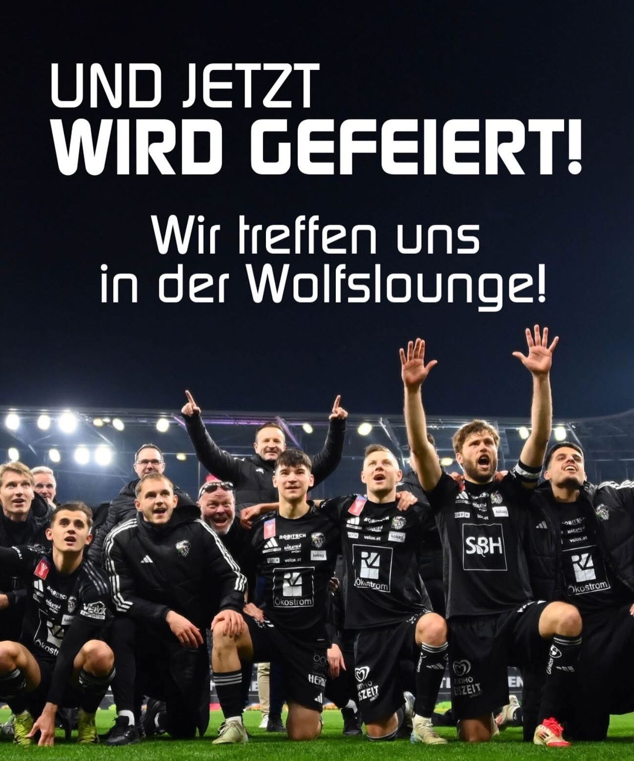 Eine Gruppe von Männern in schwarzen Trikots mit Logos feiert auf einem Sportfeld. Sie lächeln und heben ihre Hände. Der Textüberlagerung lautet: 'Und jetzt wird gefeiert! Wir treffen uns in der Wolfslounge!'