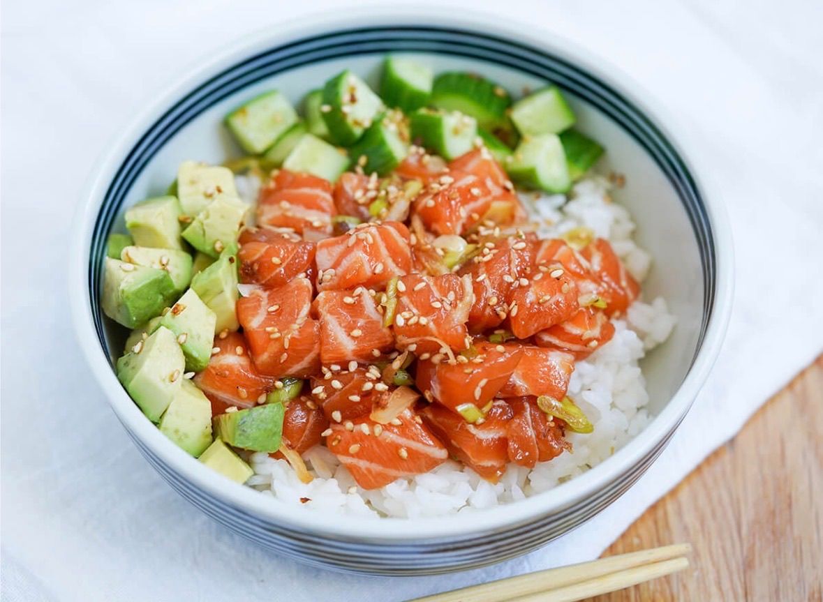 Ein Teller Sushi mit Lachs, Avocado und Gurke. Das Gericht ist mit Sesam und Frühlingszwiebeln garniert.