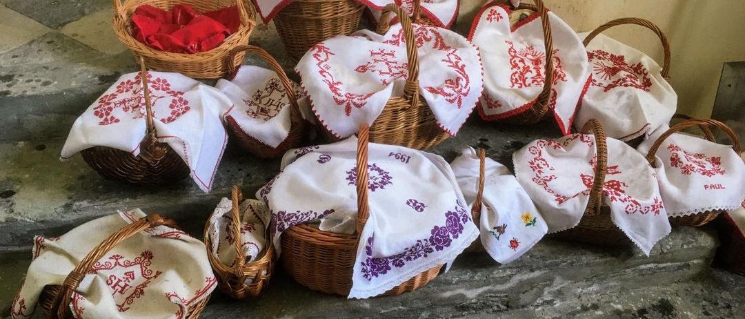 Eine Sammlung kleiner Weidenkörbe steht auf dem Boden, jeder enthält ordentlich gefaltete weiße Tücher mit roter Stickerei und einige mit roten Tüchern.