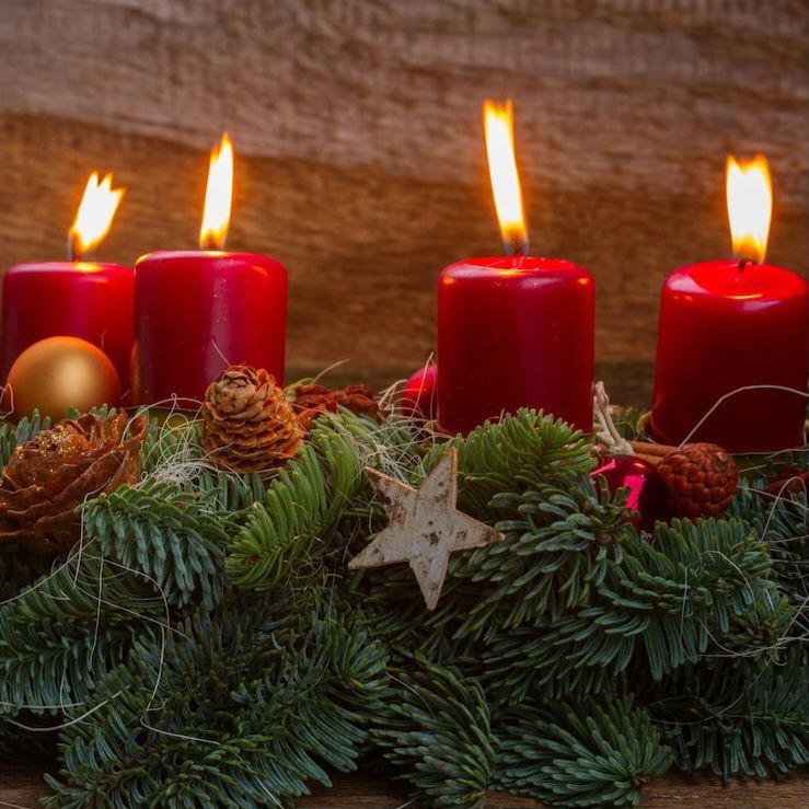 Ein Kranz aus Tannenzweigen und roten Kerzen mit Ornamenten, einschließlich einer goldenen Kugel und einem Stern, steht auf einer Holzoberfläche.
