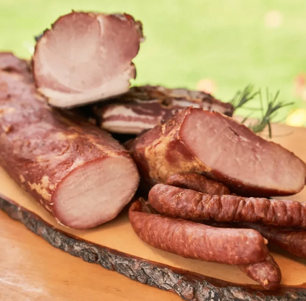 Ein Holzbrett mit verschiedenen Fleischsorten, einschließlich Würsten, Schinken und Speck, liegt auf einer Holzoberfläche.