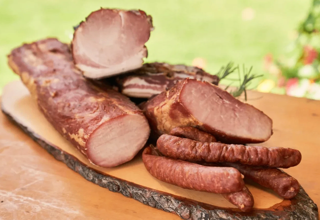 Ein Holzbrett mit verschiedenen Fleischsorten, einschließlich Würsten, Schinken und Speck, liegt auf einer Holzoberfläche.