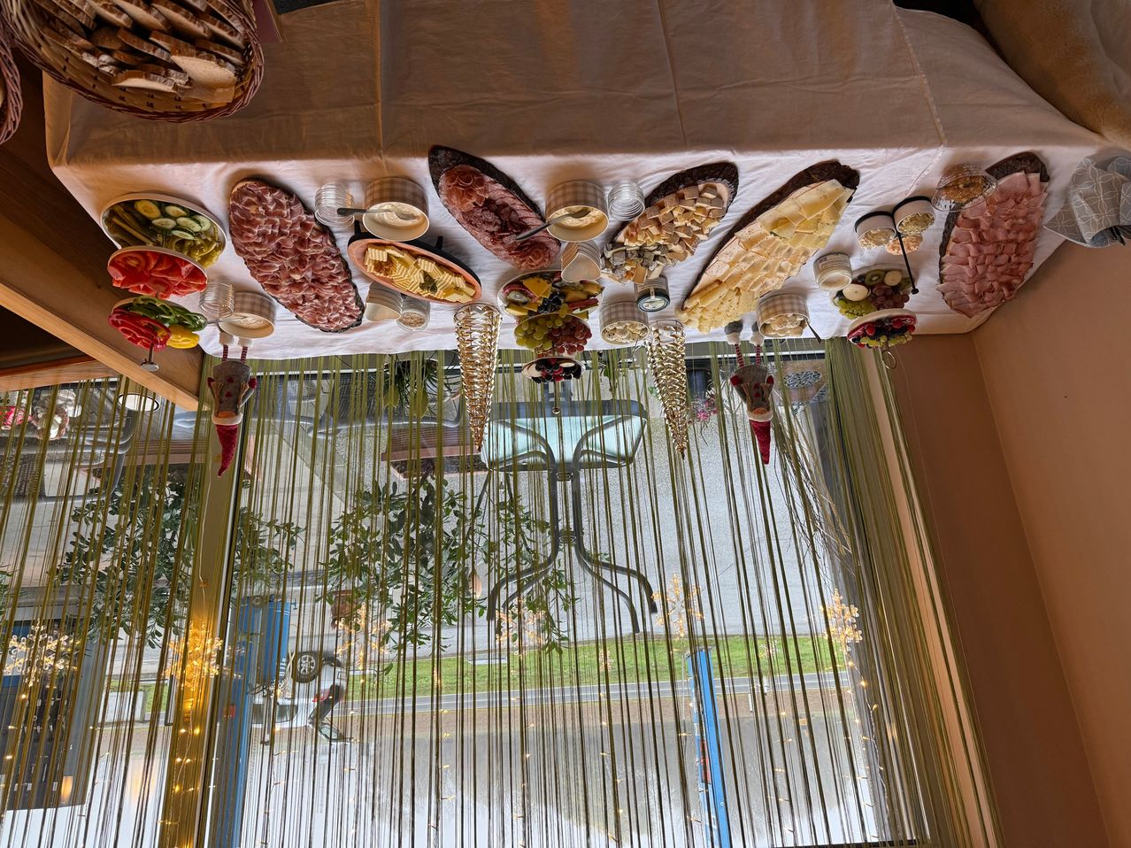 Eine festliche Tischdekoration mit verschiedenen Gerichten auf einer weißen Tischdecke, geschmückt mit dekorativen hängenden Früchten und Gemüse, beleuchtet durch Lichter.