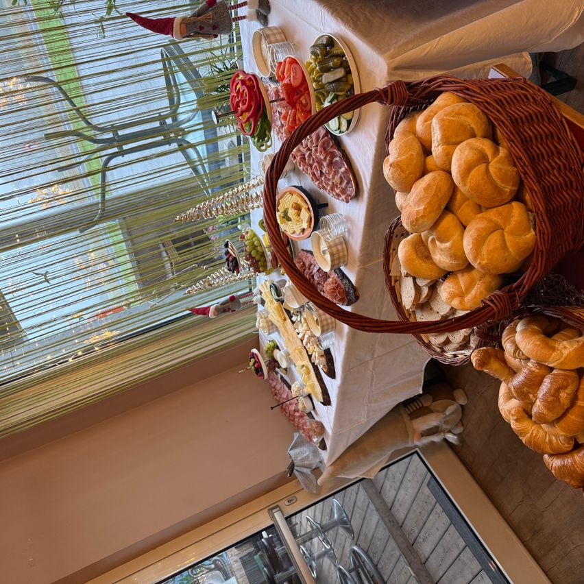Ein festlicher Tisch mit einer Vielzahl von Speisen, einschließlich Fleisch, Gemüse und Brot, in der Nähe eines Fensters mit Weihnachtsdekoration.