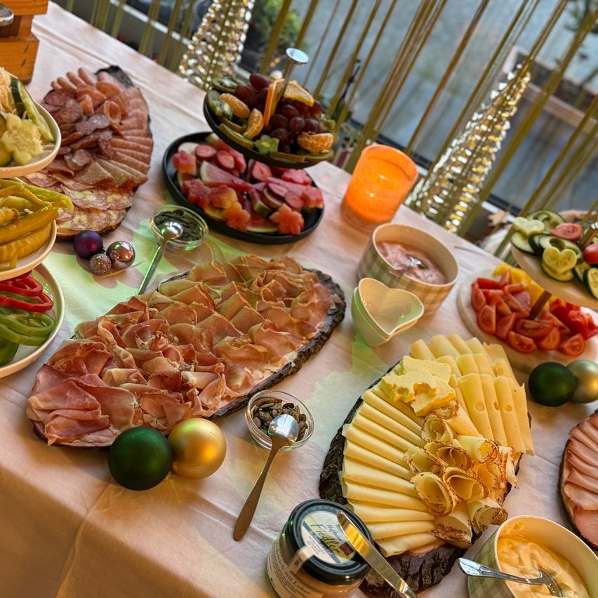 Ein Tisch ist mit einer Auswahl an Fleisch, Käse und Früchten gedeckt. Es gibt dekorative Ornamente und eine Kerze auf dem Tisch.