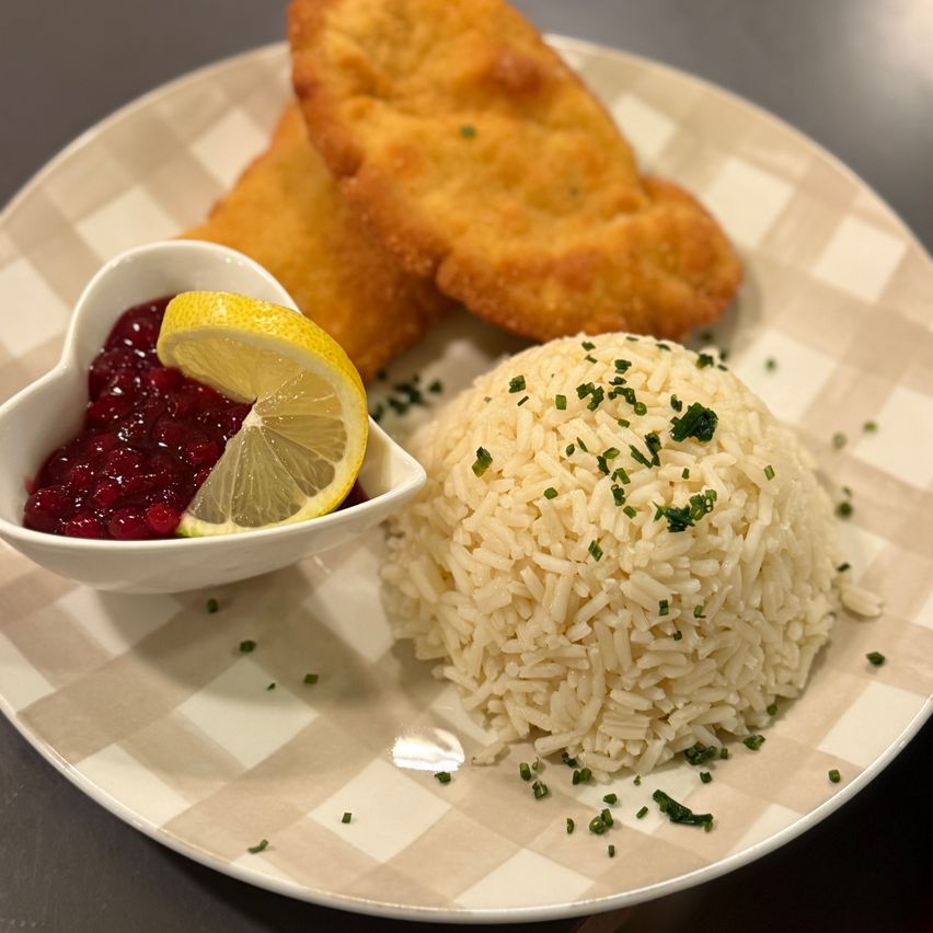 Ein Teller mit Reis, gebratenem Fisch und einer herzförmigen Schüssel mit Cranberry-Sauce und Zitronenscheibe.