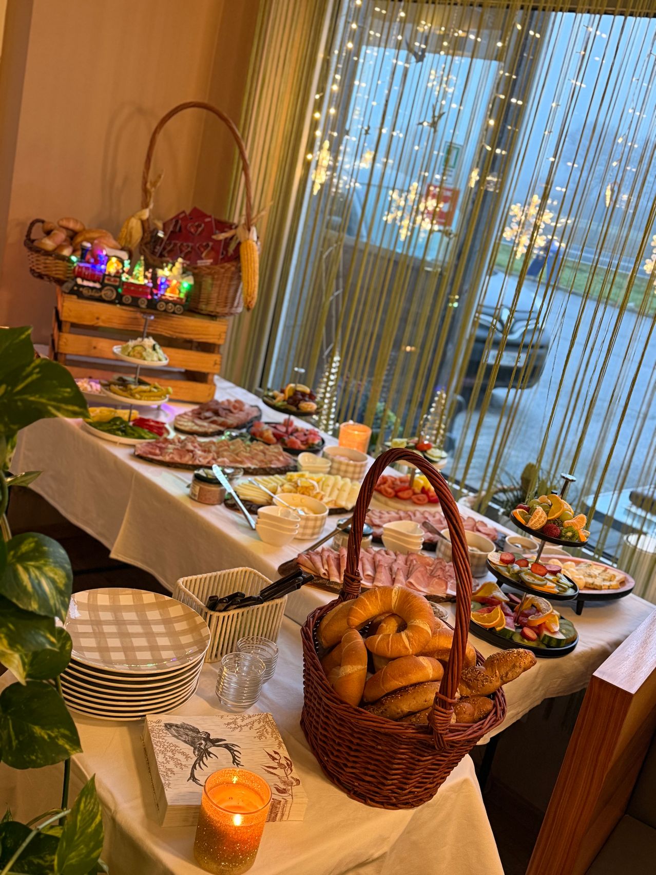 Ein Tisch ist mit einer Auswahl an Speisen gefüllt, darunter Brot, Fleisch, Obst und Gemüse. Teller, Gläser und Besteck sind ebenfalls vorhanden. Ein Korb mit Brot steht im Vordergrund.