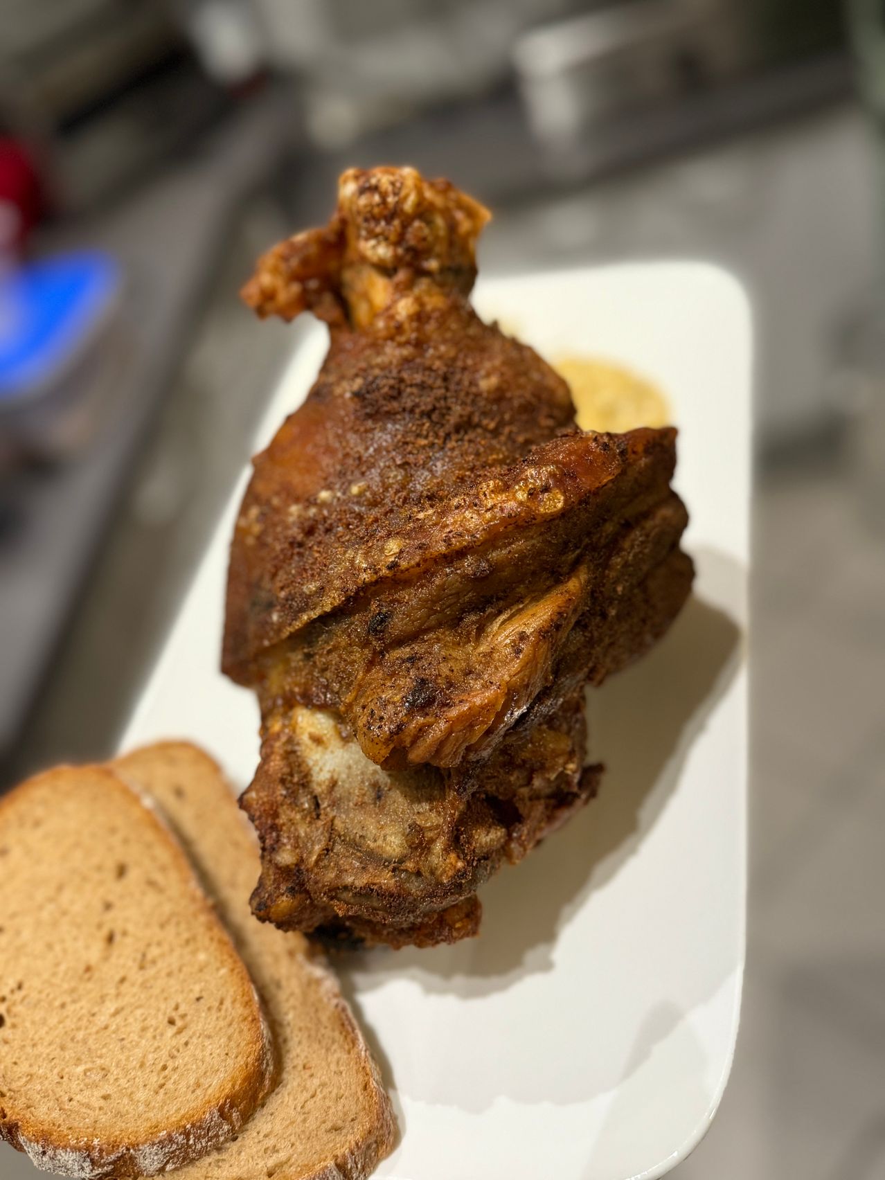 Ein Teller mit knusprigem gebratenem Fleisch und Brotscheiben auf einem weißen Teller, möglicherweise Schweineknöchel mit Senf und anderen Beilagen.