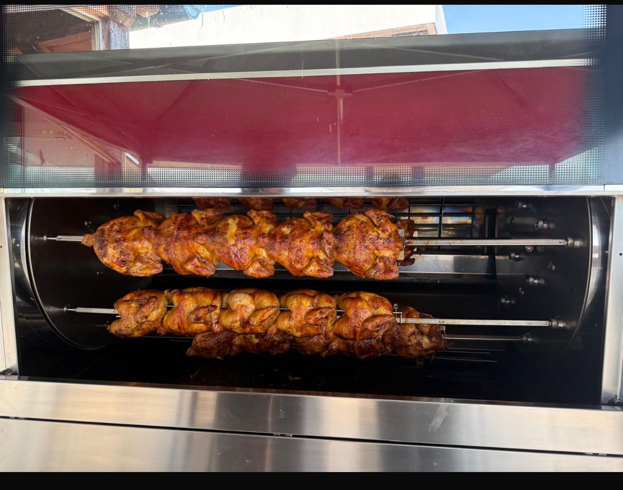 Ein kommerzieller Drehspießofen mit zwei Gestellen gebratener Hühner. Das obere Gestell hat größere Stücke, während das untere kleinere hat. Beide Gestelle drehen sich auf ihren Spießen.