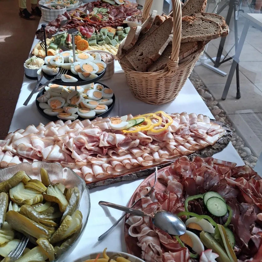 Ein langer Tisch voller verschiedener Lebensmittel, einschließlich Fleisch, Eier, Gemüse und Gurken, mit einem Korb mit Brot auf der Seite.