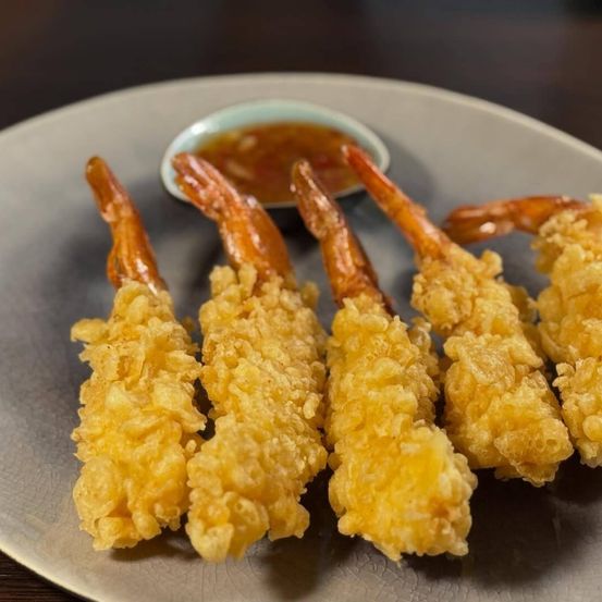 Ein Teller mit knusprigen Garnelen-Tempura mit Dip-Sauce, präsentiert auf einer Holzoberfläche.