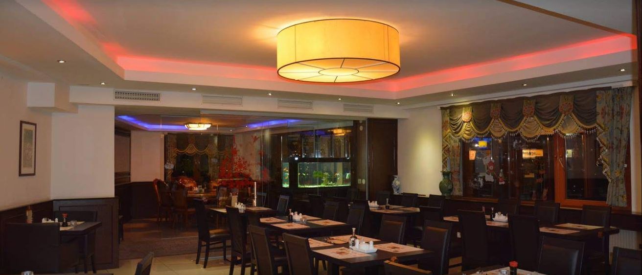 Ein Restaurant-Interieur mit runden Deckenleuchten. Tische und Stühle sind mit Tellern, Salz- und Pfefferstreuer aufgestellt. Ein Aquarium mit Fischen ist an der Wand.