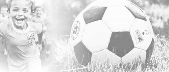 A child runs towards a soccer ball on a grassy field, wearing a soccer team jersey. The ball has a black and white pattern.