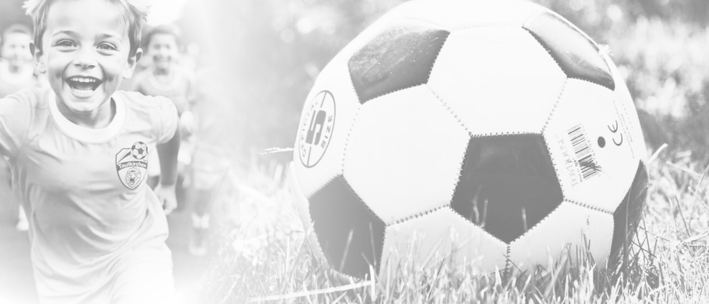 Ein Kind rennt auf einen Fußball auf einem Rasenfeld zu, trägt ein Trikot der Fußballmannschaft. Der Ball hat ein schwarz-weißes Muster.