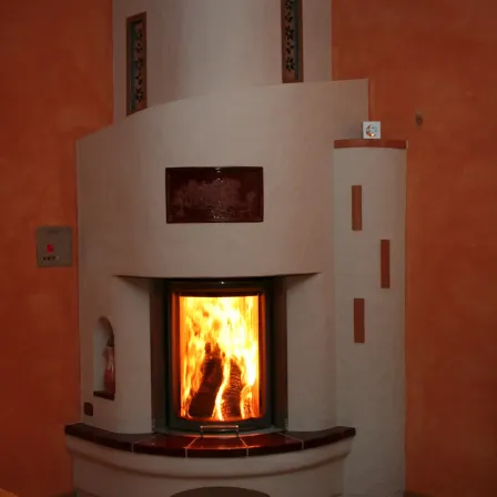 Ein moderner Kamin mit einer hellen orangefarbenen Flamme steht an einer orangefarbenen Wand. Der Kamin hat eine Glastür und dekorative Elemente an den Seiten.