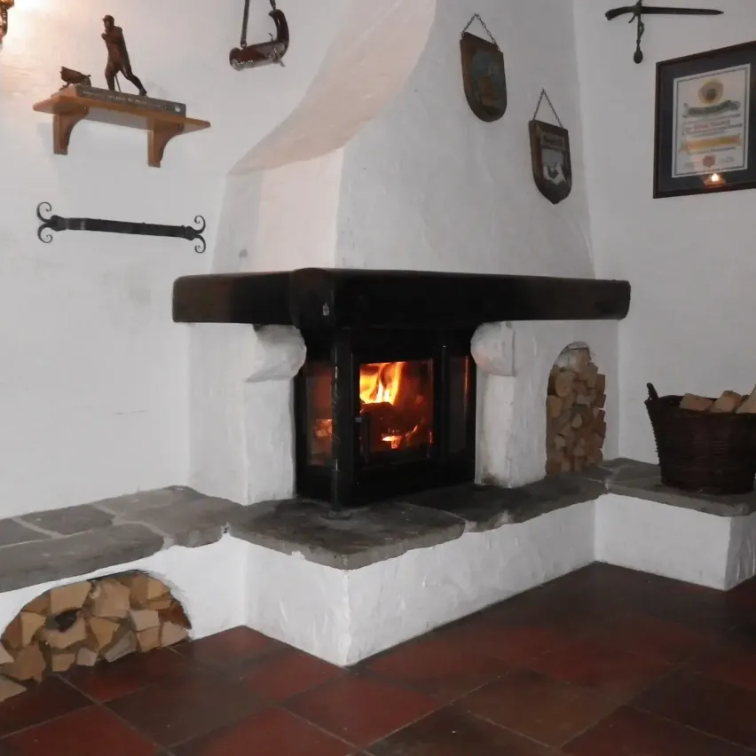 Ein gemütlicher Raum mit einem Kamin, einem Holzregal und einem Holzkorb mit Brennholz. Im Kamin brennt ein Feuer.
