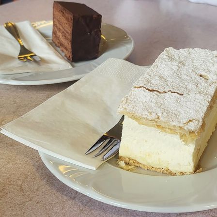 Zwei Dessertplatten: eine mit einer Scheibe Sahnekuchen bestreut mit Puderzucker, die andere mit einem Schokoladenkuchen.