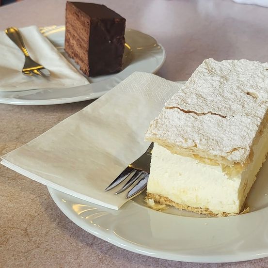 Zwei Dessertplatten: eine mit einer Scheibe Sahnekuchen bestreut mit Puderzucker, die andere mit einem Schokoladenkuchen.