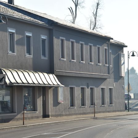 Ein graues Gebäude mit vielen Fenstern und einem Metallvordach am Ladeneingang. Ein Straßenlaterne steht auf dem Bürgersteig.