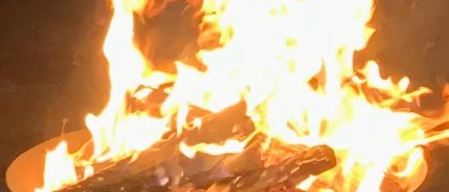 Ein Feuer brennt hell in einer Metallschale und wirft flackerndes Licht und Wärme in die Nacht.