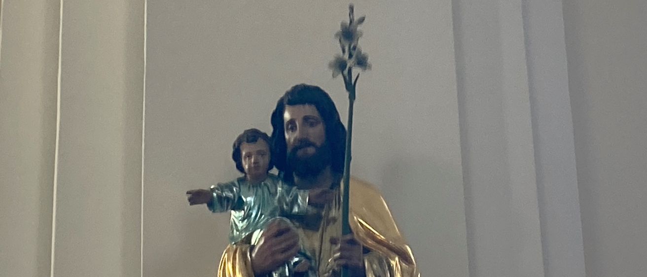 Eine goldene Statue eines Mannes, der ein kleines Kind in den Armen hält. Der Mann ist in goldenen Gewändern gekleidet und hält eine Lilie.