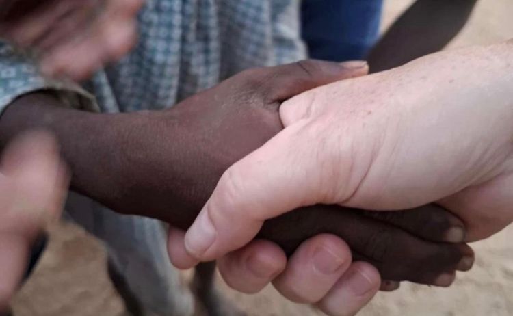Mehrere Hände sind zusammengepresst, möglicherweise in einem Kreis, mit einer Hand einer Person im Vordergrund rechts.