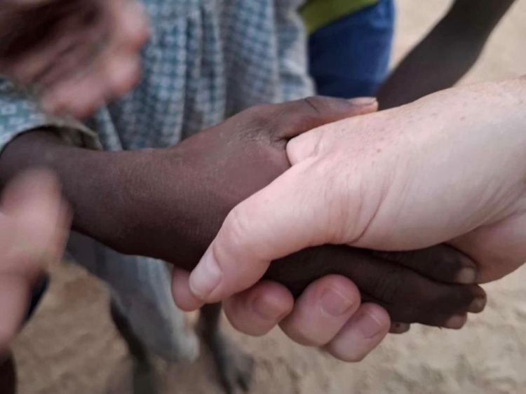 Mehrere Hände sind zusammengepresst, möglicherweise in einem Kreis, mit einer Hand einer Person im Vordergrund rechts.