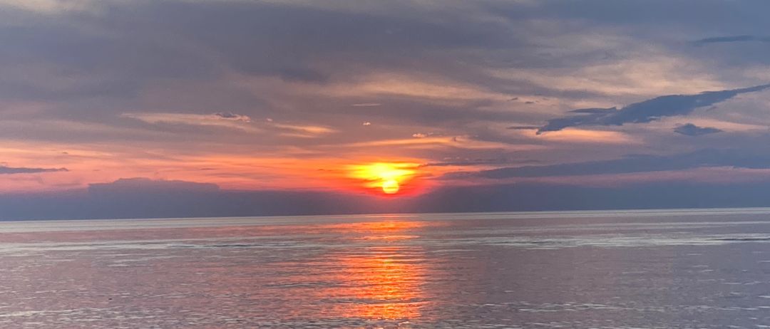 Ein Sonnenuntergang über dem Meer, mit warmen orangefarbenen und rosa Farbtönen, die den Himmel erhellen und sich auf der Wasseroberfläche spiegeln.